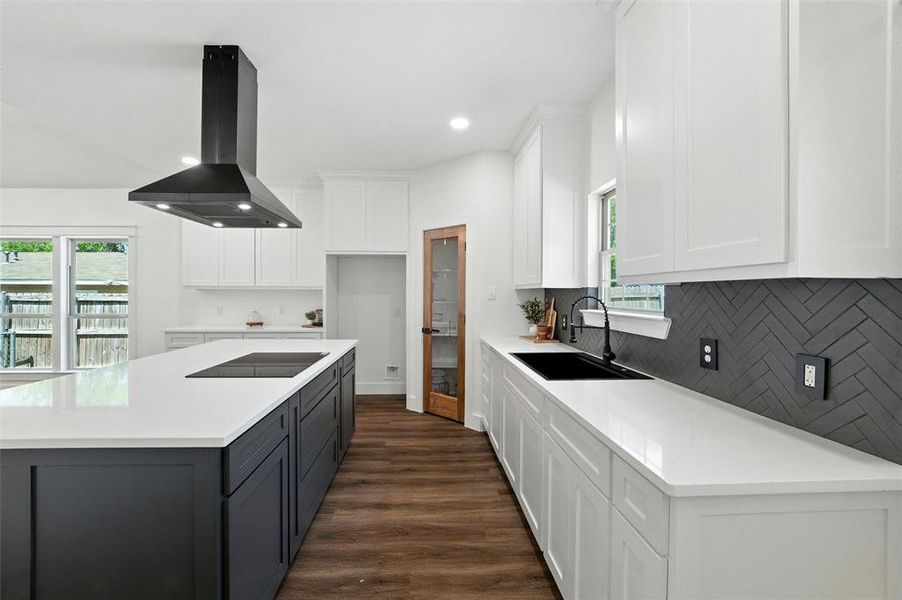 Kitchen with island exhaust hood, black electric stovetop, backsplash, white cabinetry, and a center island