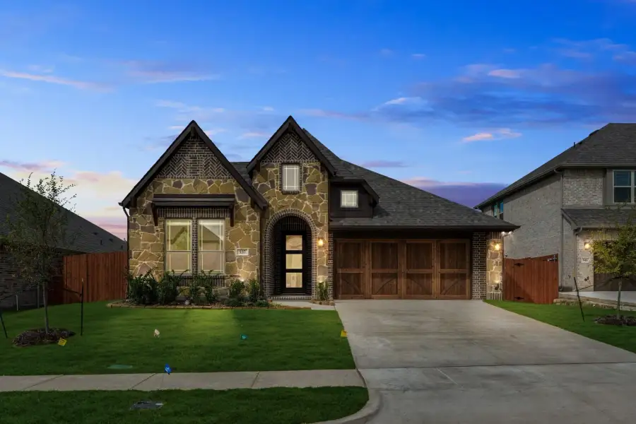 Single-story home with stone and brick exterior, arched entry, two-car garage, and front lawn at dusk
