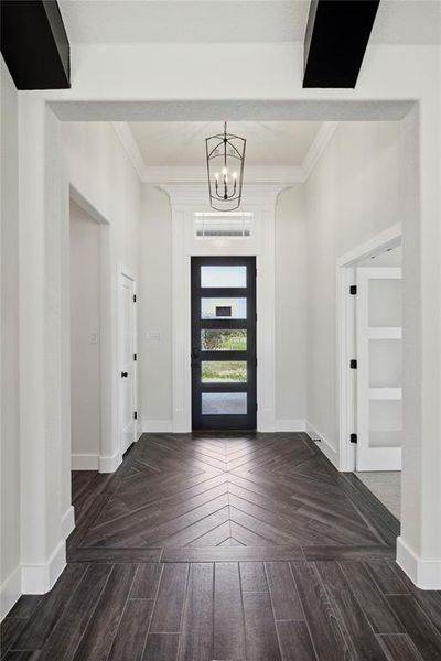 Entryway with crown molding, dark parquet flooring, and a notable chandelier