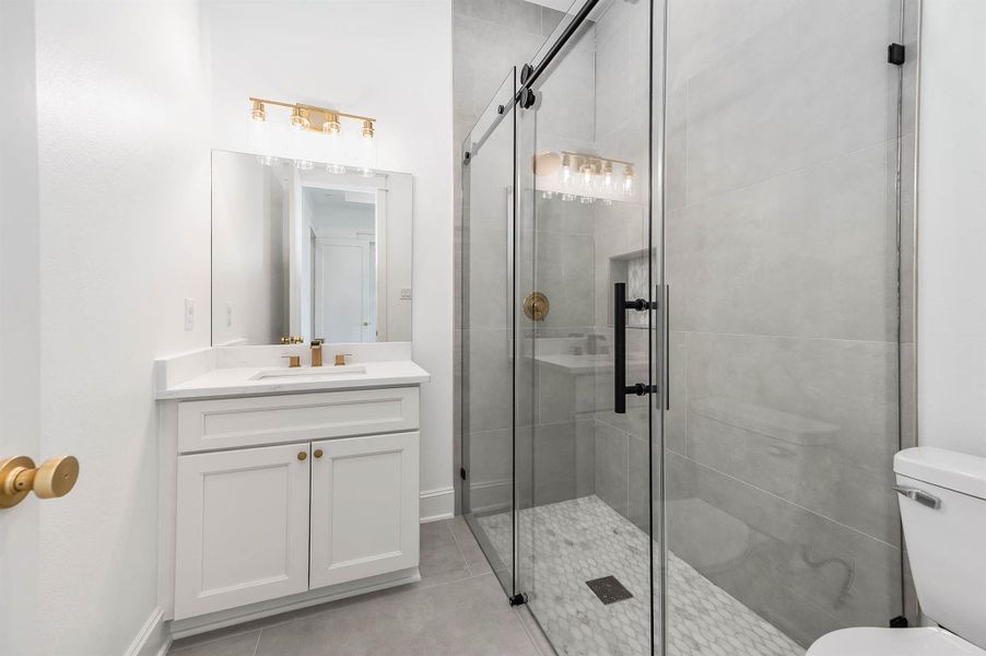 Private bathroom connected to the bedroom, featuring a walk-in shower, white vanity, and gold accents throughout.