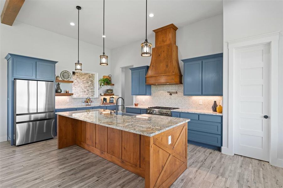 Spacious kitchen featuring a large wood-finish island with a stone-finish countertop, blue cabinetry, a wood-finish range hood, stainless steel appliances, and light wood-finish flooring