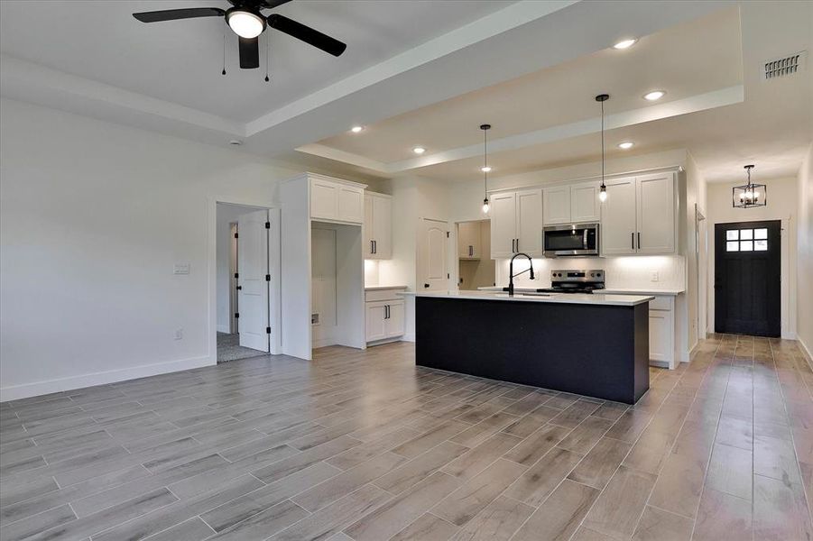 Kitchen with light hardwood / wood-style floors, stainless steel appliances, ceiling fan with notable chandelier, and a kitchen island with sink