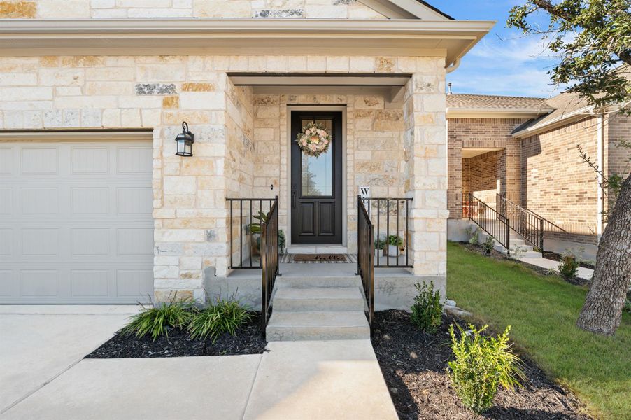 Property entrance featuring stone siding, a lawn, an attached garage, and driveway Property entrance featuring stone siding, a lawn, an attached garage, and driveway