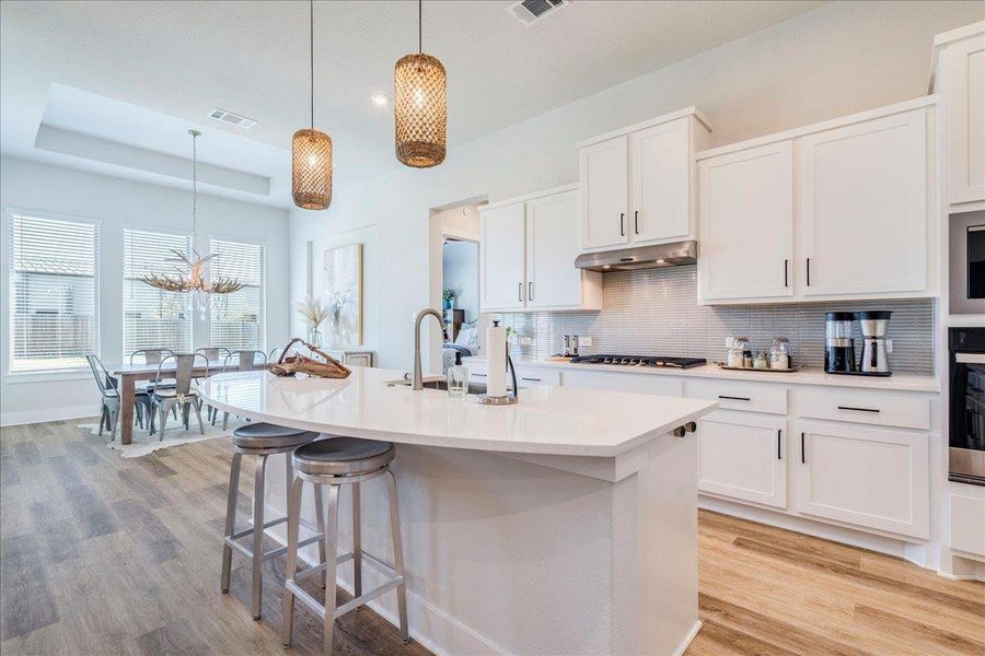 Kitchen with white cabinets, light wood finished floors, oven, a kitchen island with sink, and a kitchen bar Kitchen with white cabinets, light wood finished floors, oven, a kitchen island with sink, and a kitchen bar