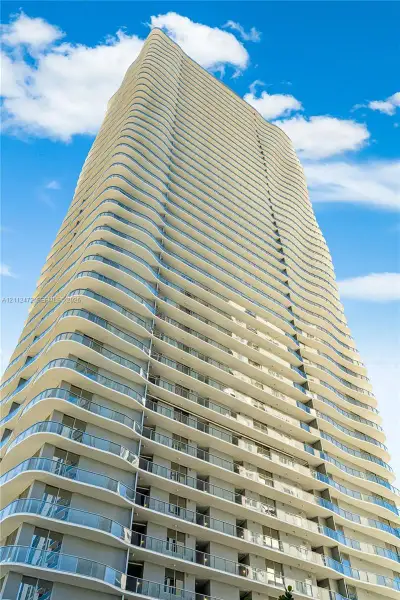 High-rise building featuring a curvilinear architectural design, recessed balconies, glass railings, and expansive exterior windows