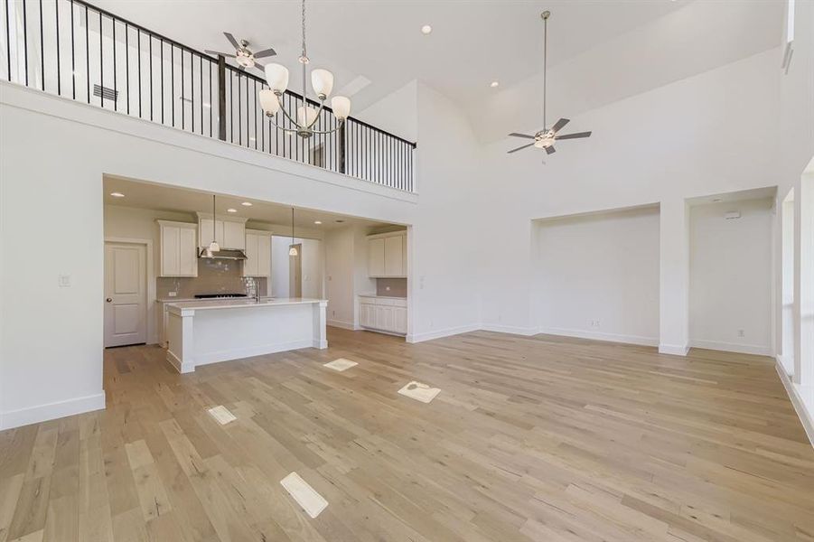Unfurnished living room featuring a ceiling fan, light wood-style floors, a high ceiling, recessed lighting, and a chandelier Unfurnished living room featuring a ceiling fan, light wood-style floors, a high ceiling, recessed lighting, and a chandelier