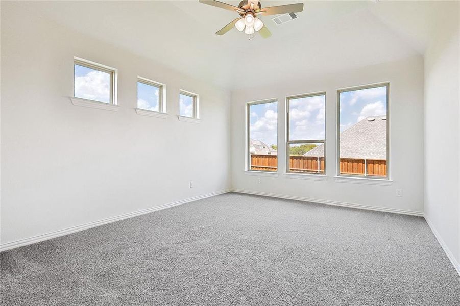 Carpeted spare room featuring ceiling fan, lofted ceiling, and plenty of natural light