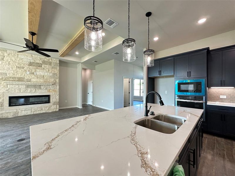 Kitchen with dark wood finished floors, dark cabinetry, pendant lighting, light stone countertops, and wall oven Kitchen with dark wood finished floors, dark cabinetry, pendant lighting, light stone countertops, and wall oven