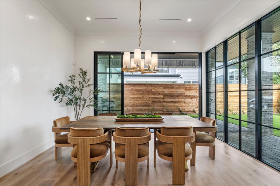 The dining room, framed by the home’s hallmark steel windows, including this four-panel sliding door. A large table and chairs fit easily here for the perfect dinner party! Hardwoods and high ceilings evoke fancy dining ambience. The Aimee chandelier adds pop!