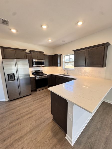 kitchen equipped with all stainless-steel appliances included, quartz kitchen countertops with an overhang & ceramic tile backsplash kitchen equipped with all stainless-steel appliances included, quartz kitchen countertops with an overhang & ceramic tile backsplash