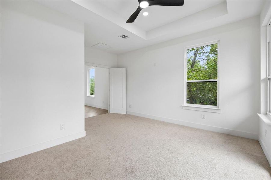 Spacious room featuring neutral carpet flooring, white painted walls, and a tray ceiling with a ceiling fan Spacious room featuring neutral carpet flooring, white painted walls, and a tray ceiling with a ceiling fan