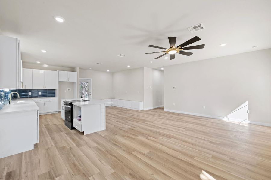 Kitchen featuring a center island with sink, white cabinets, open floor plan, light wood-style flooring, and electric range Kitchen featuring a center island with sink, white cabinets, open floor plan, light wood-style flooring, and electric range