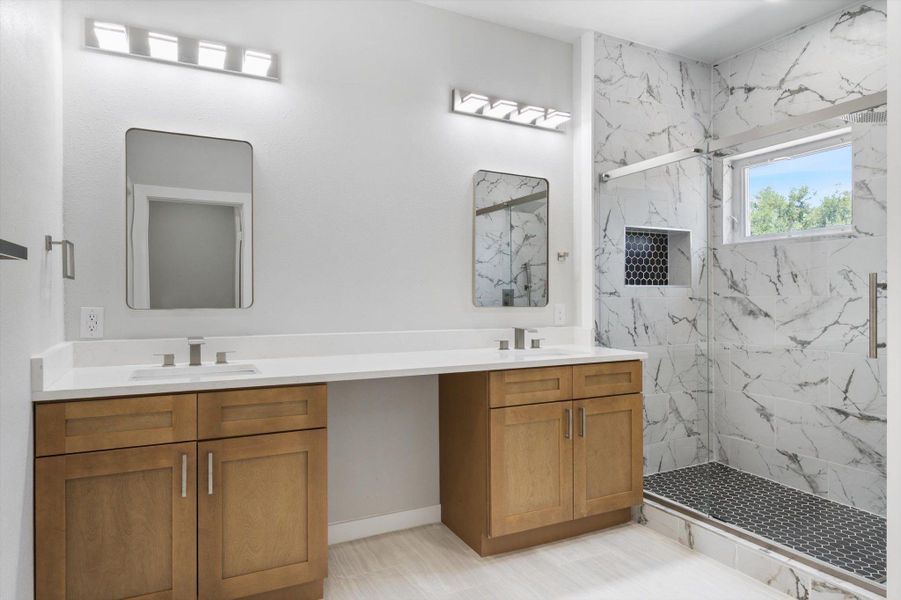 A well-appointed primary bathroom showcases a double vanity with ample counter space and a modern glass-enclosed shower.