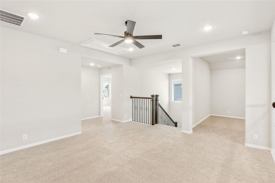 Open upstairs loft with carpet flooring, ceiling fan, and iron staircase railing