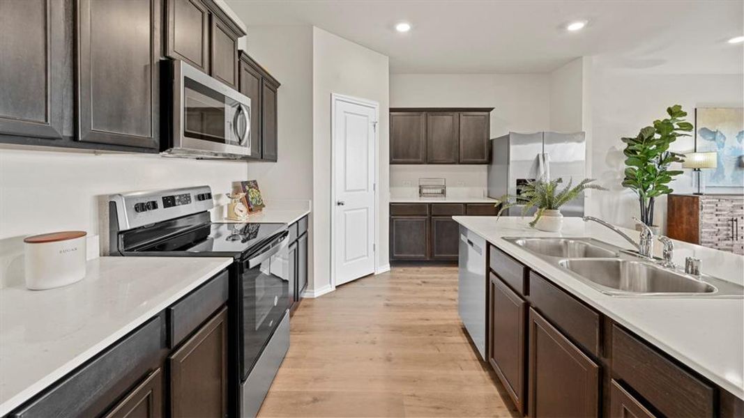 The kitchen features dark wood cabinetry, light countertops, and stainless steel appliances including a refrigerator, oven, and microwave The kitchen features dark wood cabinetry, light countertops, and stainless steel appliances including a refrigerator, oven, and microwave
