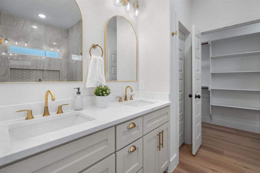 Full bath featuring double vanity, light wood-style floors, a tile shower, and a spacious closet