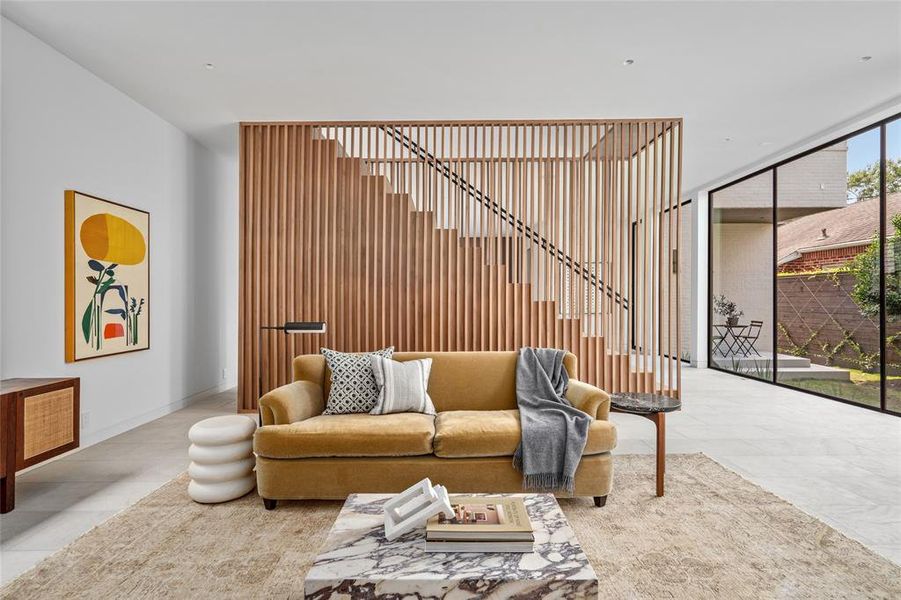 Showcasing a seamless open floor plan, the beautifully designed living room effortlessly flows into the kitchen and bar area located just behind the custom slatted walnut staircase. The large windows bring in abundant natural light and the layout creates a perfect blend of function and style.