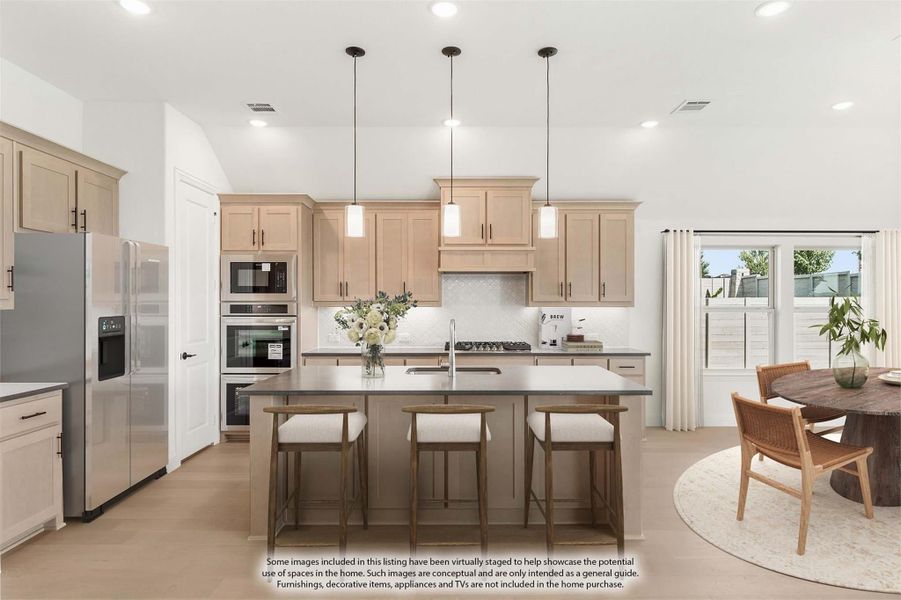 Kitchen with light wood cabinets, large island with dark countertop, pendant lights, and stainless steel appliances