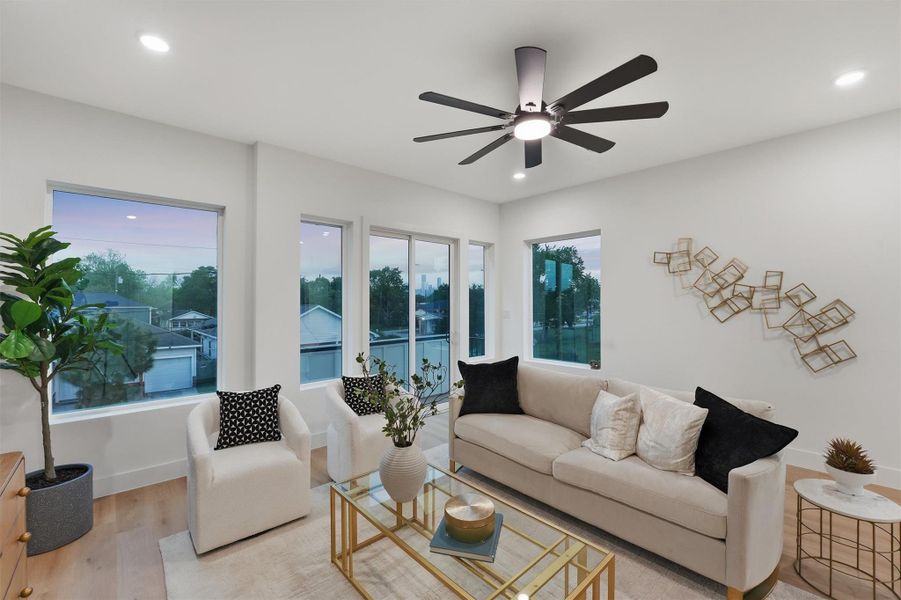 Bright, modern living room featuring wood-look flooring, oversized windows, recessed lighting, a contemporary ceiling fan, and a stylish seating area filled with natural light for an open, airy feel.