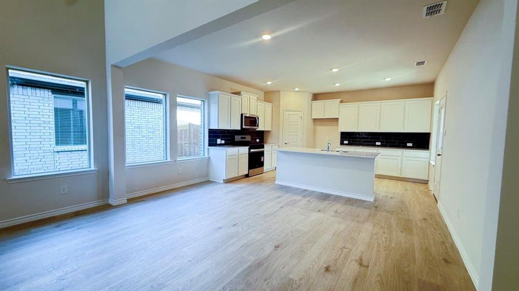 Kitchen featuring decorative backsplash, white cabinetry, appliances with stainless steel finishes, light wood-type flooring, and recessed lighting
