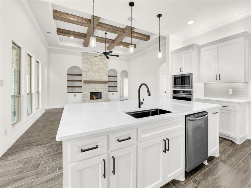 Kitchen featuring wood finish floors, coffered ceiling, white cabinetry, open floor plan, and a kitchen island with sink