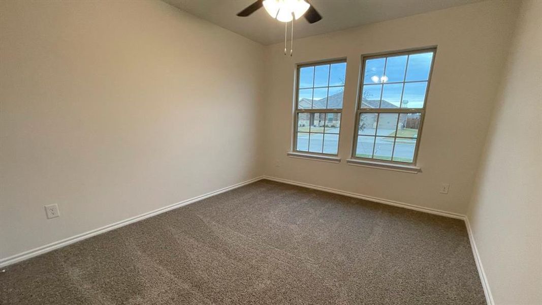 Carpeted room featuring two double-hung windows, a ceiling fan with integrated lighting, white baseboards, and neutral wall tones