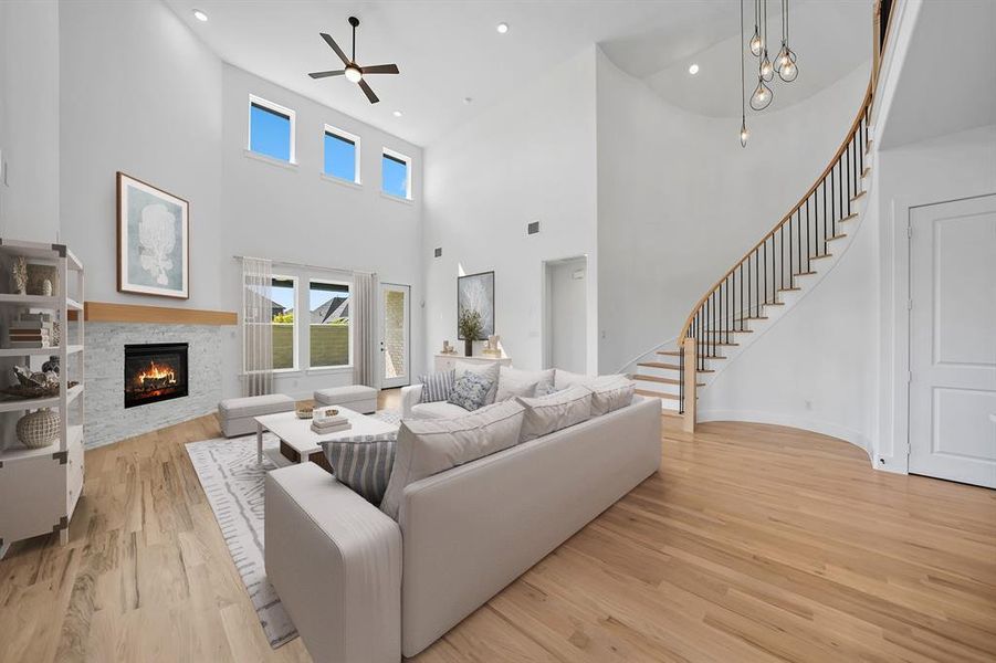 Living area featuring light wood-type flooring, stairs, a stone fireplace, a high ceiling, and recessed lighting