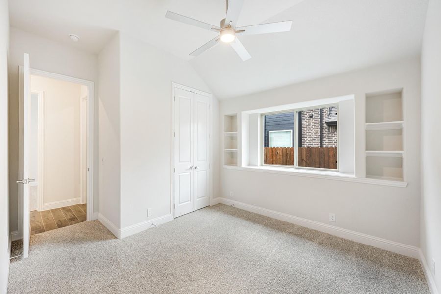 Bedroom with vaulted ceiling, ceiling fan, carpet, closet, and built-in shelves flanking a window