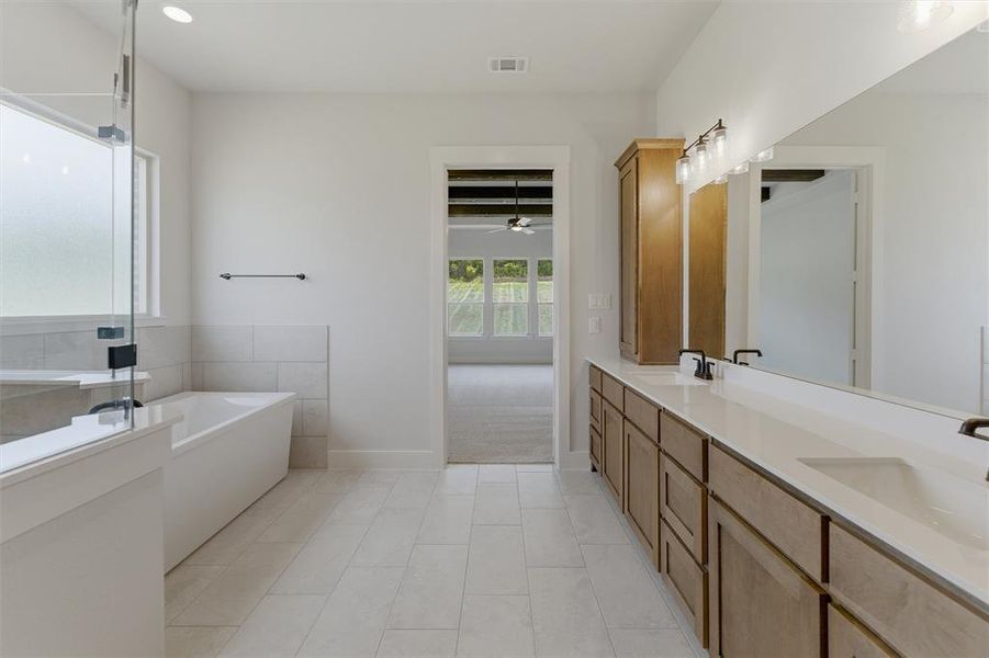 Bathroom featuring a freestanding soaking tub, clear glass shower enclosure, light-toned tile flooring, and a double vanity with ample storage