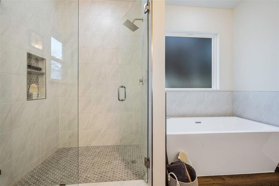 A stunning freestanding soaking tub anchors the space between shower and water closet, while the spacious walk-in shower promises resort-style indulgence. Exquisite tilework steals the show in this designer shower featuring floor-to-ceiling marble-look porcelain and chic hexagonal mosaic flooring. Frameless glass enclosure with rainfall shower head and built-in niche for storage.