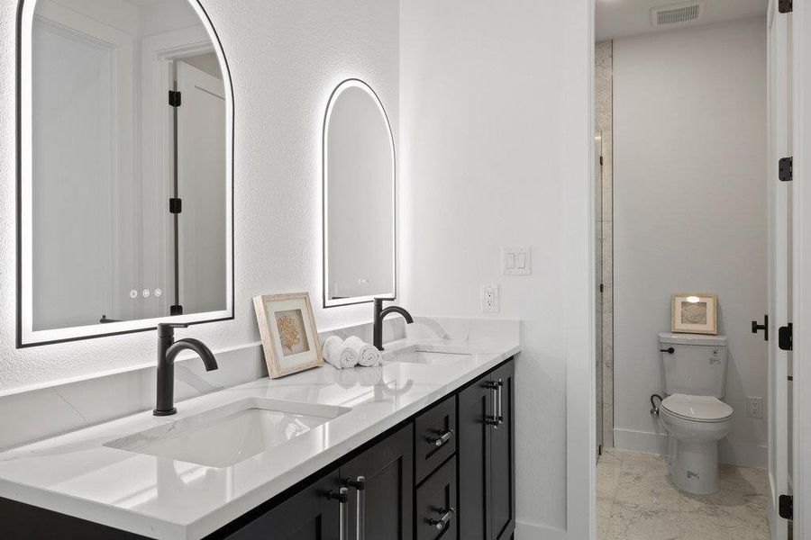 The stunning jack-n-jill bathroom features a custom dual vanity, lighted mirrors, and a private bath with the toiler and frameless glass walk-in shower.