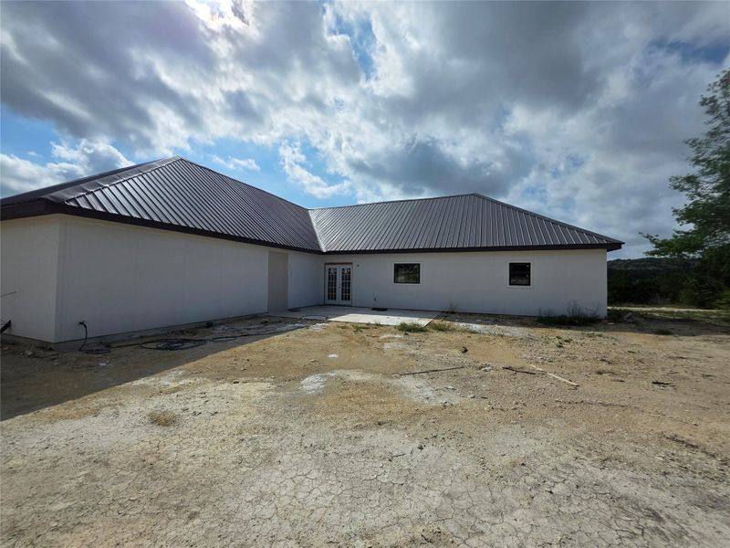 Exterior featuring a metal roof, white stucco siding, and a double patio door
