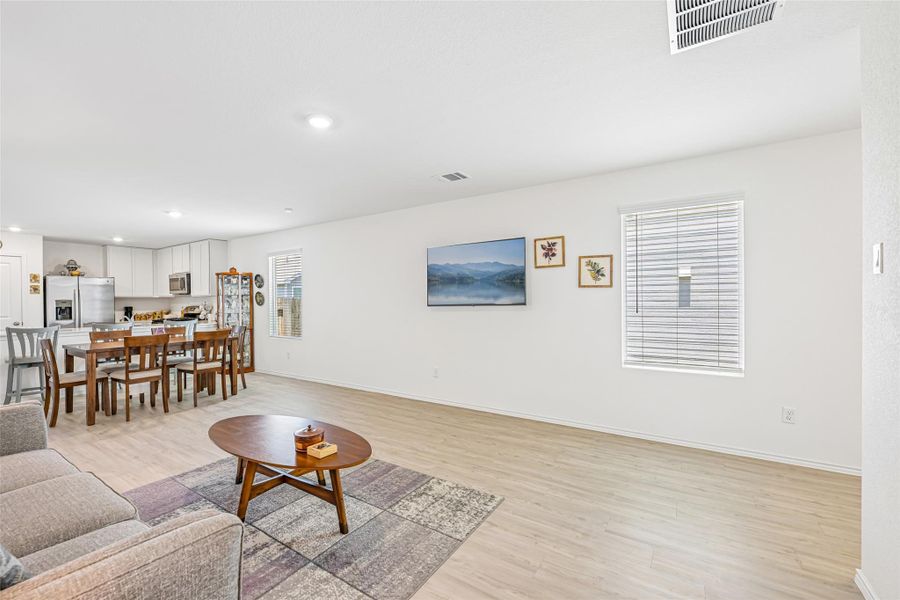 Open-concept living area featuring light wood-finish flooring, recessed lighting, white walls, and a window with blinds Open-concept living area featuring light wood-finish flooring, recessed lighting, white walls, and a window with blinds