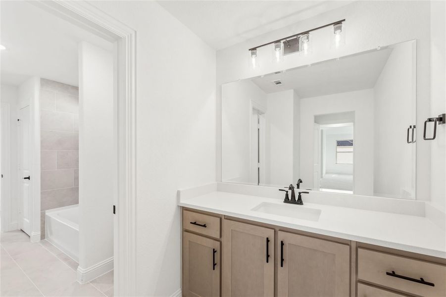 Bathroom with wood vanity, white countertop, large mirror, and separate soaking tub with tiled shower area visible