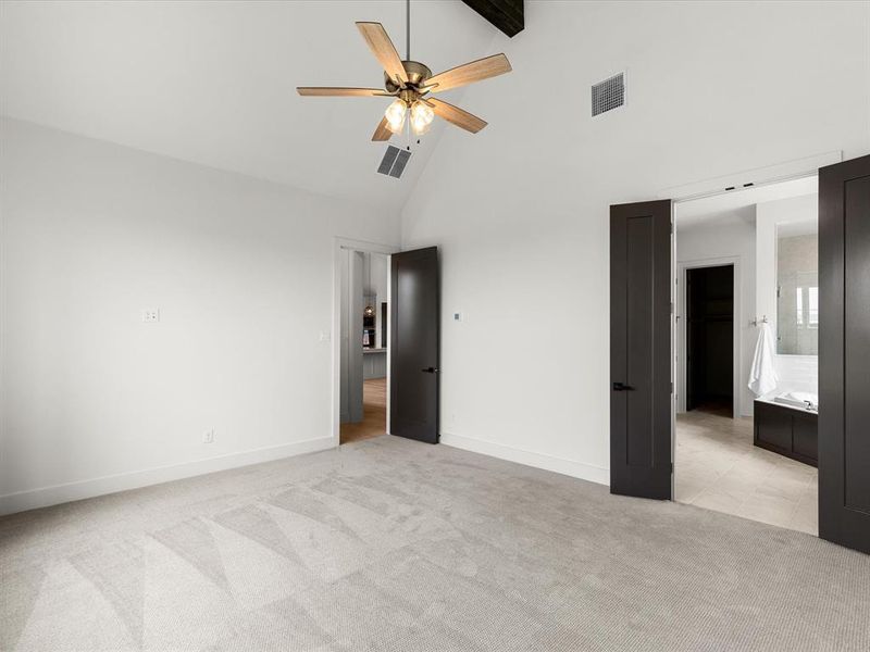 Unfurnished bedroom with light colored carpet, high vaulted ceiling, ensuite bath, a ceiling fan, and beam ceiling Unfurnished bedroom with light colored carpet, high vaulted ceiling, ensuite bath, a ceiling fan, and beam ceiling