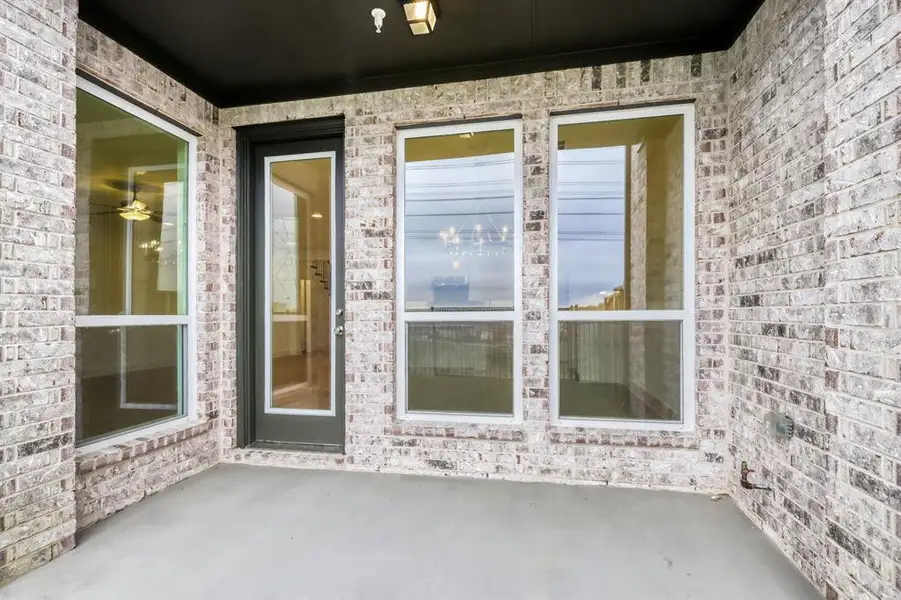 Covered patio featuring a light-toned brick exterior, multiple large windows, a full-lite glass door, and a concrete floor