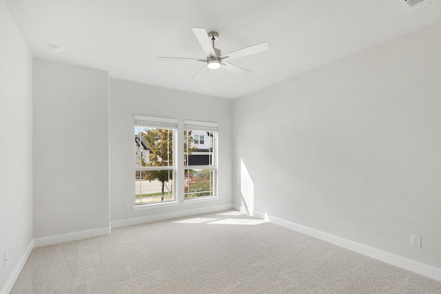 Empty bedroom with ceiling fan, carpet flooring, and double windows with natural light