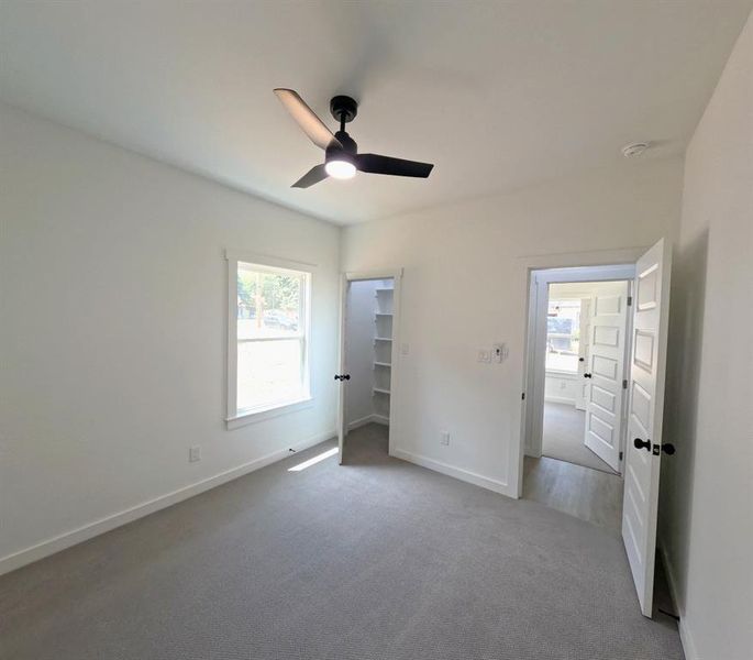 Unfurnished bedroom featuring multiple windows, a spacious closet, carpet floors, and ceiling fan Unfurnished bedroom featuring multiple windows, a spacious closet, carpet floors, and ceiling fan