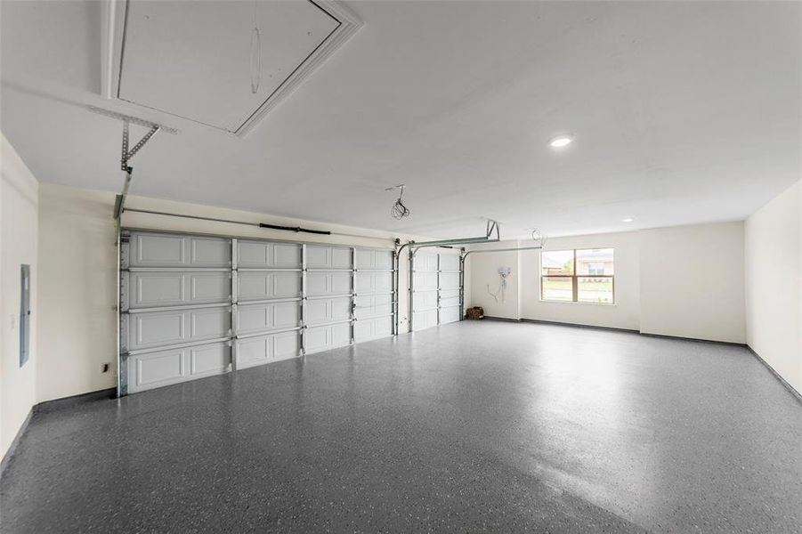 Spacious garage featuring a speckled epoxy floor, two overhead doors, recessed lighting, and a window providing natural light