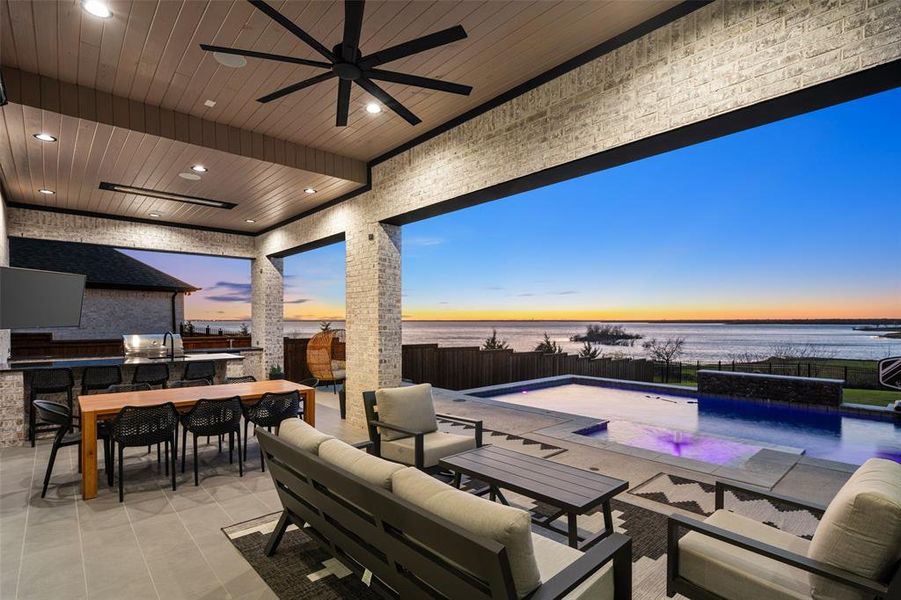 Resort-style backyard retreat featuring a stunning pool, expansive patio, and covered outdoor living area designed for both relaxation and entertaining. The outdoor kitchen and lounge space seamlessly connect to the home, while the second-floor balcony above provides an additional private vantage point to enjoy the beautiful surroundings and lake views.