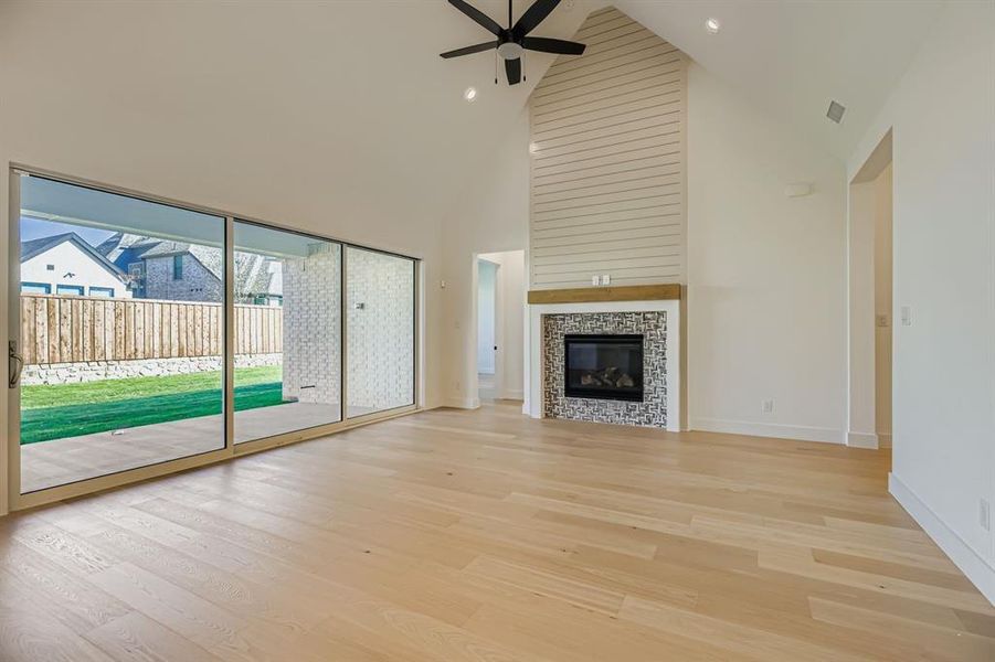 Unfurnished living room featuring high vaulted ceiling, light wood-type flooring, a tile fireplace, and ceiling fan Unfurnished living room featuring high vaulted ceiling, light wood-type flooring, a tile fireplace, and ceiling fan