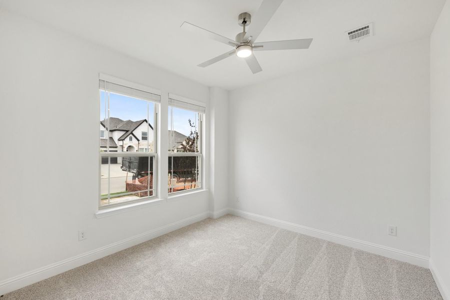 Empty bedroom with carpet flooring, ceiling fan, and two windows overlooking neighboring homes