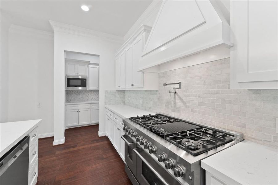 Modern kitchen featuring white cabinetry, stainless steel appliances, a gas cooktop, and marble countertops with a subway tile backsplash, complemented by rich, dark wooden flooring.