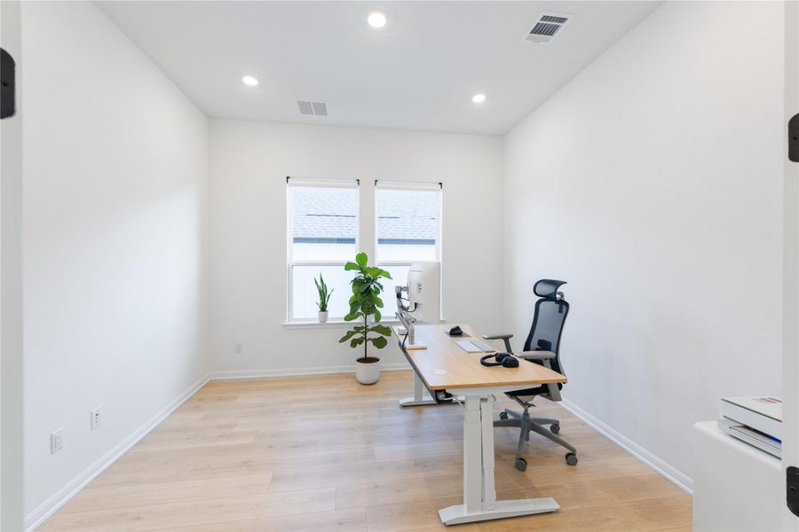 Office with light wood-style floors and recessed lighting
