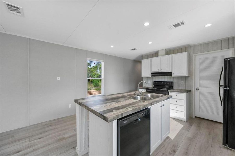 Kitchen with visible vents, black appliances, light wood-type flooring, and a sink