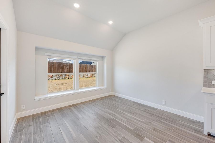 Empty room with vaulted ceiling, wood-look tile floors, and a large window overlooking a fenced backyard Empty room with vaulted ceiling, wood-look tile floors, and a large window overlooking a fenced backyard