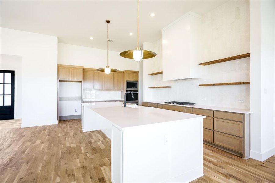 Kitchen with appliances with stainless steel finishes, backsplash, pendant lighting, a center island with sink, and light hardwood / wood-style flooring