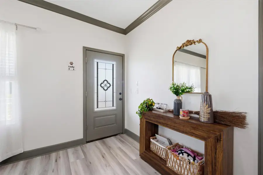 This inviting entryway features a decorative glass door, sleek wood flooring, and a stylish console table with a mirror. The space is bright and welcoming, ideal for greeting guests.