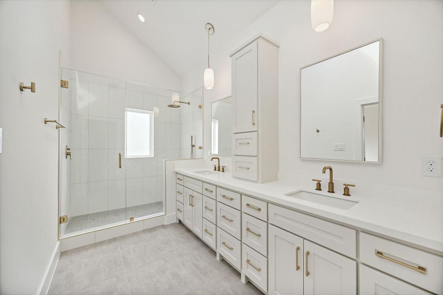 Luxurious primary bath features a vaulted ceiling, sky light, frameless glass walk in shower, dual vanities with coordinating hardware, designer faucets, plumbing accessories, modern light fixtures and separate toilet room