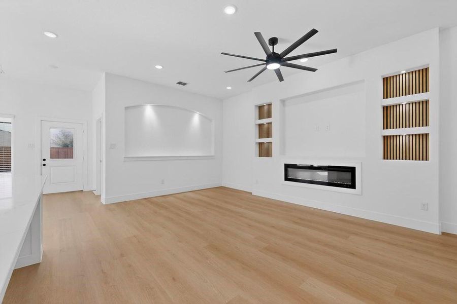 Unfurnished living room with built in features, a ceiling fan, light wood finished floors, a glass covered fireplace, and recessed lighting